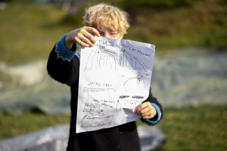 En ung gutt viser fram tegningene sine, ute i godt vær.